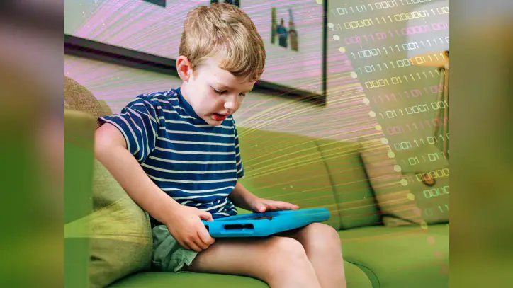 Elementary-aged child is sitting on sofa while working/playing on tablet computer at home, May 2025.
