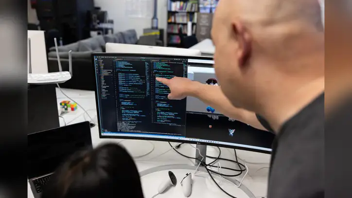 over the shoulder image of a professor and student looking at a monitor of code