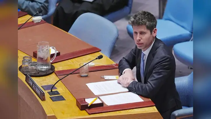 OpenAI CEO Sam Altman sits on a blue chair at a long wooden desk at the United Nations General Assembly.