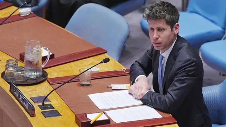 OpenAI CEO Sam Altman sits on a blue chair at a long wooden desk at the United Nations General Assembly.