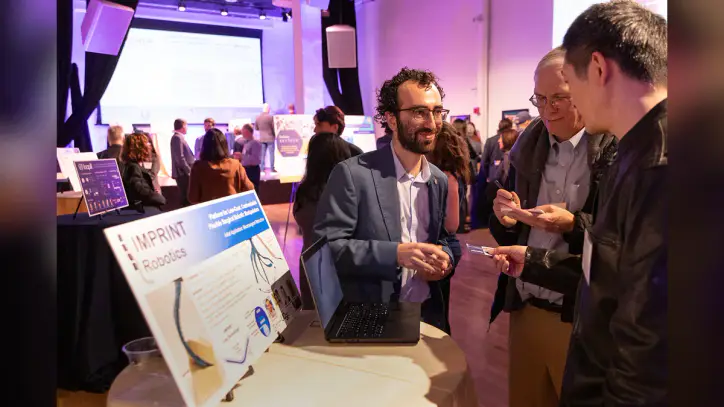 A group of people gather at a mixer event to discuss new business ventures. They're gathered near a robotics organization.