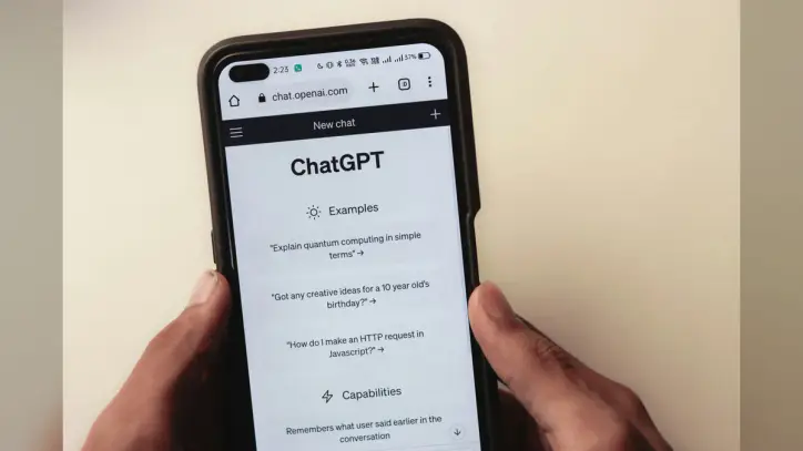 A person holds a cell phone open to a ChatGPT webpage, which is prompting the user to ask a series of questions.